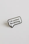 Enamel pin with 'i'd rather be skiing.' text on a light gray background