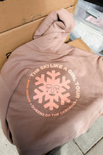Pink hoodie with graphic design and text on a cardboard surface